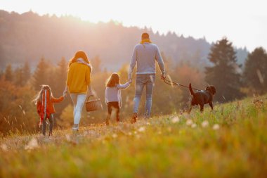 Günbatımında sonbahar doğada bir zeminde oturan iki küçük çocuklu mutlu genç aile portresi.