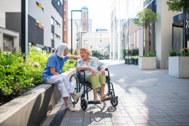 Tekerlekli sandalyedeki kıdemli hasta, kadın bakıcısıyla konuşuyor..