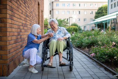 Tekerlekli sandalyedeki kıdemli hasta, kadın bakıcısıyla konuşuyor..