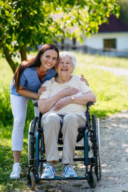 Tekerlekli sandalyede yaşlı bir hastayla yürüyen kadın hemşire..
