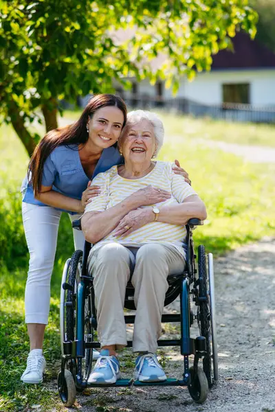 Tekerlekli sandalyede yaşlı bir hastayla yürüyen kadın hemşire..
