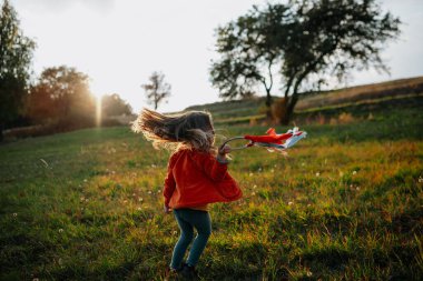 Küçük kız elinde kurdele, gün batımında çayırda yürüyor..