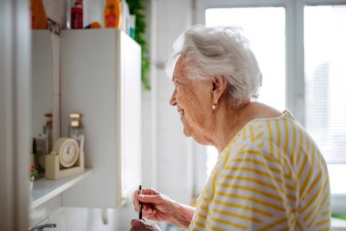 Yaşlı kadın banyo aynasında tenini ve görünüşünü kontrol ediyor..