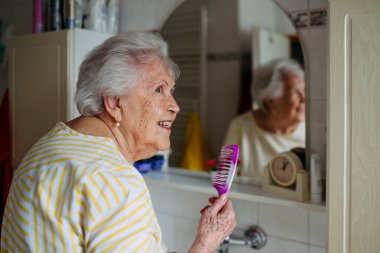 Yaşlı kadın banyoda saçını tarıyor..