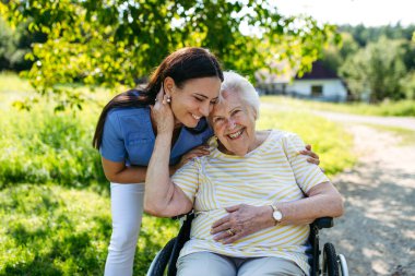 Tekerlekli sandalyede yaşlı bir hastayla yürüyen kadın hemşire..