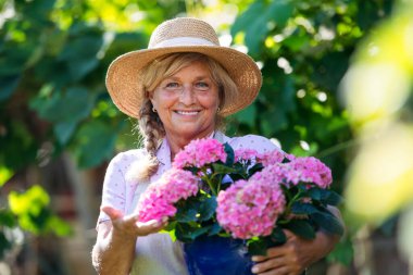 Bahçede elinde pembe çiçeklerle gülümseyen bahçıvan.