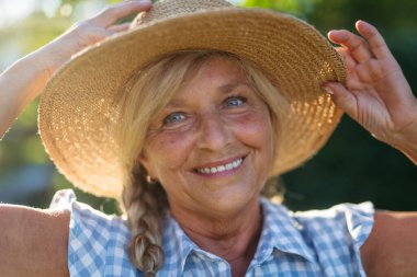 Mutlu yaşlı kadın bahçede güneşli bir günün tadını çıkarıyor, şapka takıyor..
