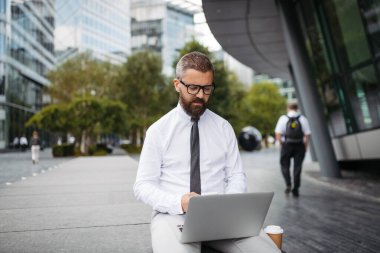 Dizlerinin üzerinde çalışan yakışıklı iş adamı, parkta oturuyor..