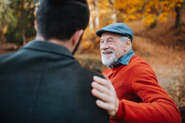 Dedem ve torunum parkta bankta oturup sarılıyorlar. Sonbahar mevsimi.