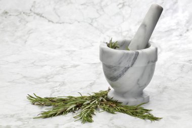 Rosemary herbs and a mortar and pestle on grey and white marble kitchen surface