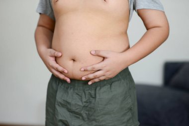 Şişman göbekli şişman bir çocuk elleriyle karnını tutuyor..