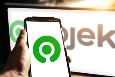 Pringsewu, Lampung; 21 Kasım 2023; ekranda Gojek logo uygulaması olan android telefonu tutan bir adam, ekranın önünde optik bir işaret fişeği. Yazı