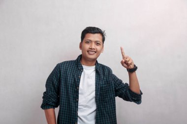 Ekose elbiseli olgun bir adam kamerayı işaret ediyor. Bir parmağı yukarıda, beyaz arka planda.