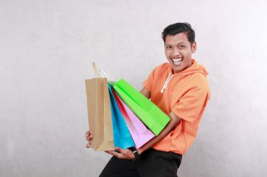 Turuncu t-shirt giyen Asyalı olgun bir adam kağıt torba taşıyor, neşeli ifadeli bakkaliye, mutlu, soyutlanmış beyaz arka plan