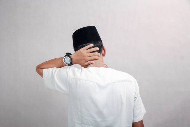 Müslüman bir adam arkasını dönüp ağrıyan bir boynun omzunu tutarak bakar.