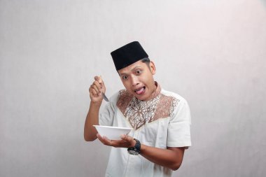 Yetişkin Müslüman adam kaseyi boşaltmak istiyor ve kaşığı tuhaf bir ifadeyle tutuyor, izole edilmiş beyaz arka plan.