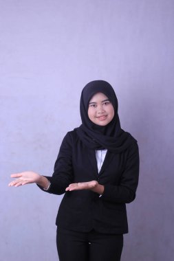 Siyah takım elbiseli genç bir kadın mor bir arka planın önünde duruyor..