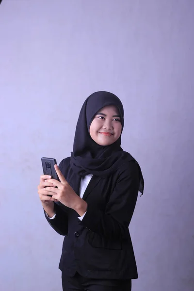 A woman in a black suit is holding a phone and smiling. potret