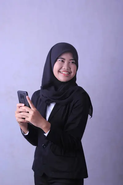 A woman in a black suit is holding a phone and smiling.
