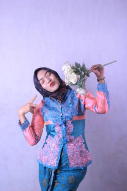 Mutlu Asyalı Endonezyalı tesettürlü kadının, elinde çiçekleri tutarken gözleri kapalı, beyaz arka planda soyutlanmış bir fotoğrafı.