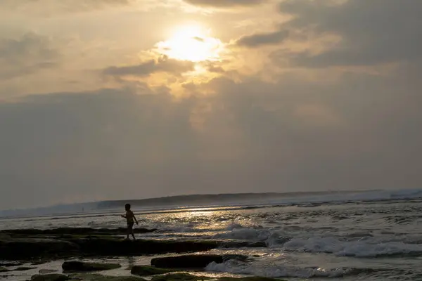 stock image silhouette of a small child on the beach against a background of waves and evening sky. optical beacon