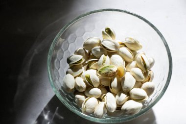 Aydınlık gölge arka planında izole edilmiş beyaz cam kasedeki fıstıklı fındık seçici odak.