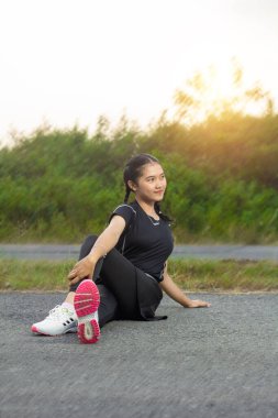 Güzel Asyalı bir kadının portresi. Her öğleden sonra parkta spor yapıyor. Doğal manzara ve gün batımıyla. Koşmadan önce sıcak bel hareketleriyle asfalt yolda oturdu.