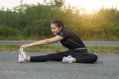 Güzel Asyalı kadın her öğleden sonra parkta egzersiz yapıyor doğa ve gün batımını seyrediyor. O, yolun asfaltına oturdu. Bu rahatlama ve vücut sağlığı için bir yaşam tarzı.