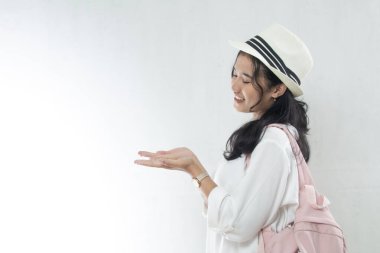 Portrait of Asian woman wearing straw hat and pink bag looking aside as if showing product in her hand, product advertising mockup copy space clipart