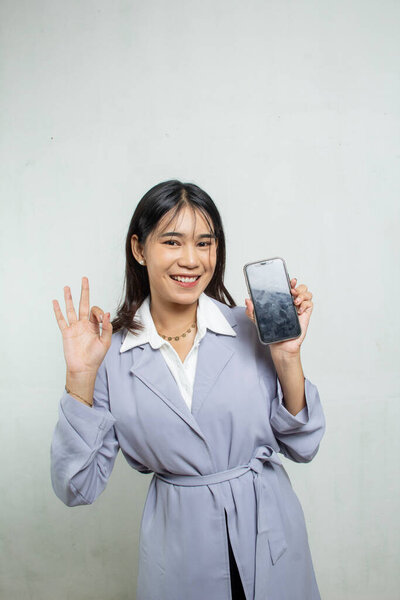 working woman standing and successful three finger greeting with news from her cell phone, light purple blue shirt, office woman advertisement, isolated white background