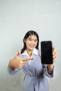 Siyah cep telefonu ekranını gösteren çalışan bir kadının kamerasına doğru üstten bakıldığında açık mavi bir gömlek giyiyor. Reklam amaçlı işçi reklamı.