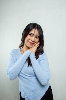 Vücudunun yarısını ayakta tutan tatlı bir Asyalı kız, beyaz bir stüdyo tarafından korunan yanağında bir el hareketiyle onu uykuya davet ediyor.