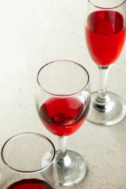 Kırmızı şurupla doldurulmuş üç şarap kadehi granit desenli bar masasında köşegen bir çizgi oluşturuyor.