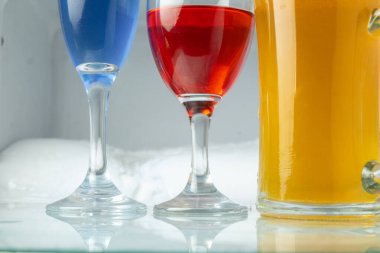 Bardaklarla renkli kokteyller, cam masa tabanı ve buz soğutucu arka plan.