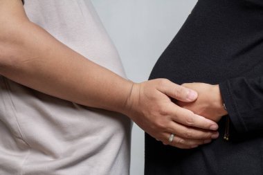Tanımlanamayan hamile bir çift birbirlerini tutuyorlar. Siyah kadın kıyafetleri ve krem erkek tişörtleri giyiyorlar. Romantik gelecekteki anne ve baba, beyaz tenli.