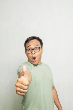 Asyalı bir adamın yüzü kameraya, yarı vücut adamına ve açık yeşil gömleğe başparmaklarıyla şaşırdı.