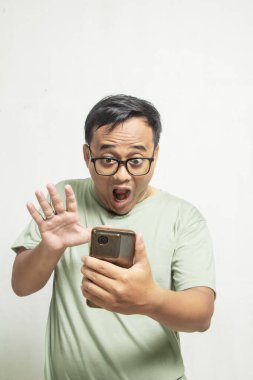 Gözlüklü Asyalı bir adamın portresi. Akıllı telefonuyla beyaz stüdyo arka planında gördüklerine bakıyor.