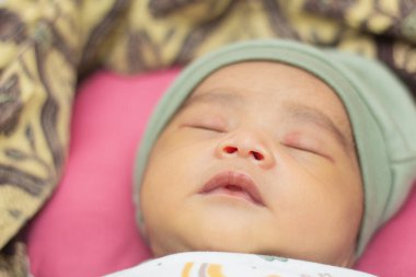 Bir haftadan az bir süre önce yeni doğmuş bir bebeğin yeşil bir şapkayla uyuması.