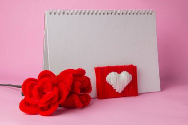 Pembe arka planda kalp şekli ve defter yakın plan ve kırmızı gül boru temizleyicisinin yanında.