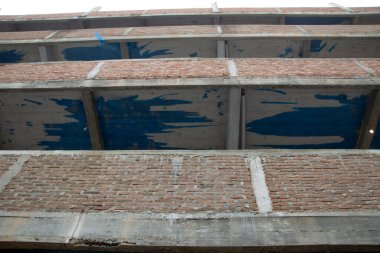 Tamamlanmamış, kırmızı tuğlalı, çok katlı bir okul binasının çitlerinin tepesinden, inşaat devam ediyor.