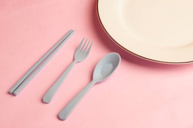 Üst görünüm çatal, kaşık, çatal, yemek çubukları gri plastik ve pembe arka planda yuvarlak tabaklar gibi.