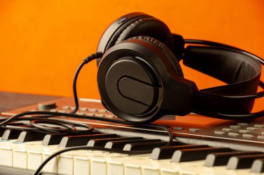 Elektronik piyano klavyesindeki kulaklıklar turuncu arka planlı sentezleyici