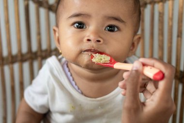 Kimliği belirlenemeyen bir kadının bebeğini evde emzirdiği fotoğraf. Bebek, dudakları kilitliyken ya da annesi tarafından emzirilmeyi reddederken bir rattan üzerine oturur..