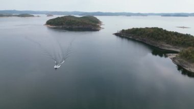 ABD 'nin Oklahoma şehrinde yüzen bir tekneyle Broken Bow Gölü' nün su yüzeyinin havadan görüntüsü. Sahilde ormanı olan kıyı şeridinin sonbahar manzarası.