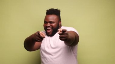 Afro-Amerikalı, pembe tişörtlü, kurnaz gülümsemeli, kameraya gülümseyen, piyangoda zafer, başarı şansı olan bir adam. Açık yeşil arka planda kapalı stüdyo çekimleri.