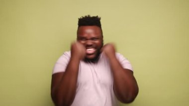 Mutlu Afro-Amerikalı adam heyecanlı bir ifadeyle ayakta duruyor, yumruklarını kaldırıyor, bağırıyor, bağırıyor evet, zaferini kutluyor, başarısını kutluyor. Açık yeşil arka planda kapalı stüdyo çekimleri