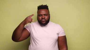 Crazy idea. African-american man showing stupid gesture, looking at camera with condemnation and blaming for insane plan, dumb suggestion. Indoor studio shot isolated on light green background.