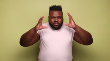 Sağlıksız, hasta, genç, sakallı, Afro-Amerikalı, pembe tişört giyen, şakak masajı yapan, baş ağrısı çeken, migren ağrısı çeken bir adam. Açık yeşil arka planda kapalı stüdyo çekimleri.