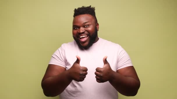 快乐兴奋的非裔美国人穿着粉色T恤在室内工作室拍摄显示大拇指向上 像一个手势 看着相机展示他的满意 浅绿色背景的孤立物 — 图库视频影像