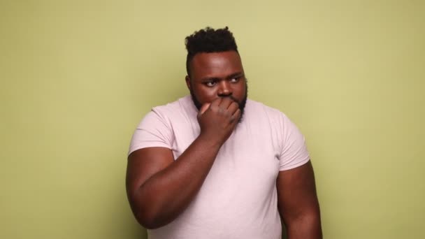 心配しているアフリカ系アメリカ人の男性は ピンクのTシャツを着て爪をかむ トラブルについて緊張し パニックになり 怖がっているのを強調した 薄い緑の背景に隔離された屋内スタジオショット — ストック動画